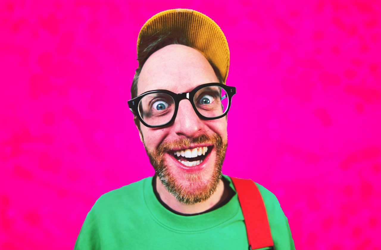 Mushy P smiling in front of a pink background